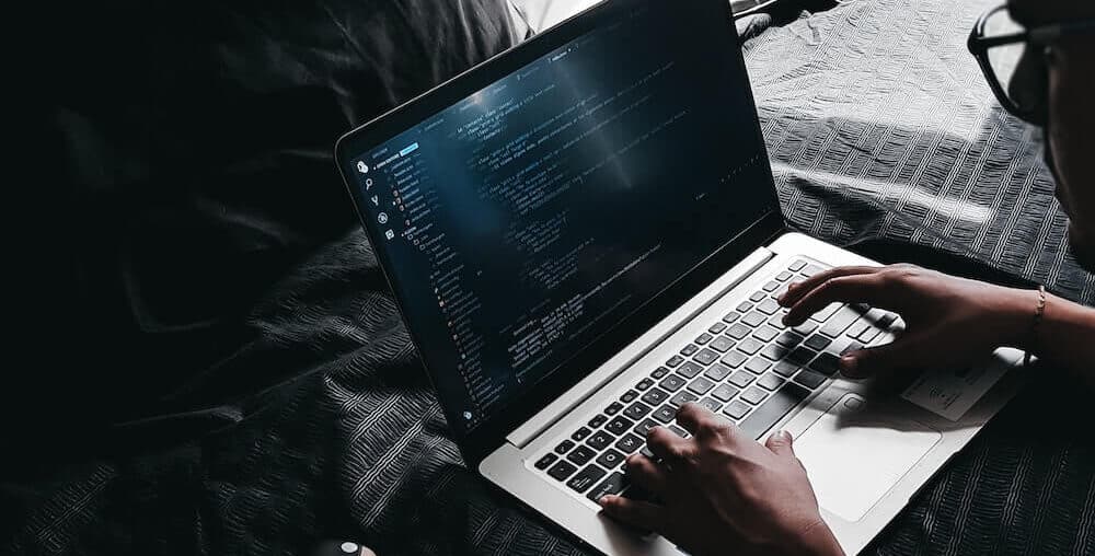 Programista tworzy kod na łóżku