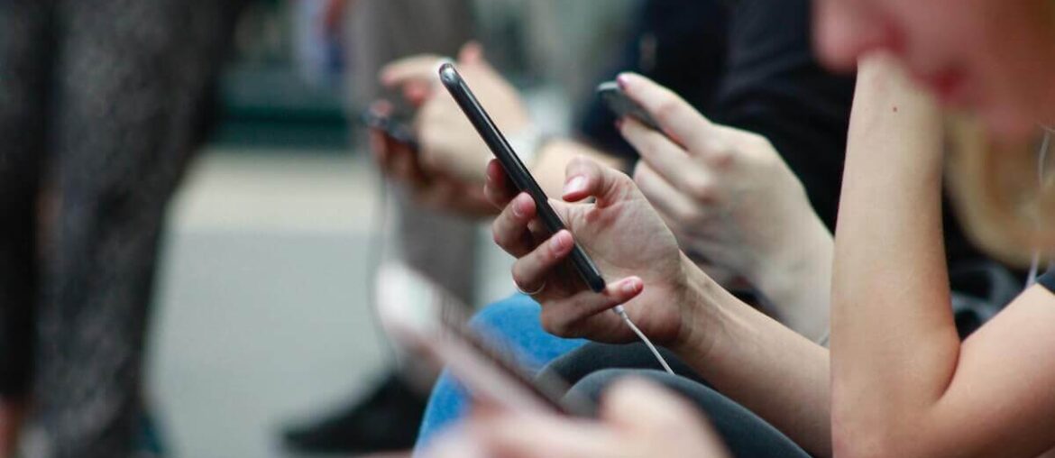 Młode osoby siedzą na powietrzu i patrzą w telefony